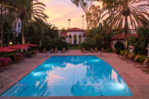 Apartment pool area at sunset with lounge chairs and surrounding buildings.