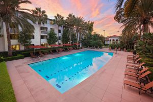 Apartment pool area at sunset with lounge chairs and surrounding buildings.