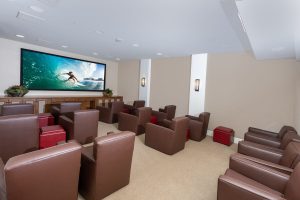 Movie lounge with brown chairs and a large wall-mounted screen.