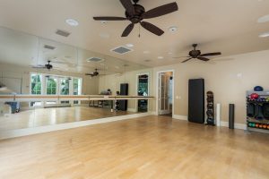 Fitness room with hardwood floors, mirrors, and ceiling fans.