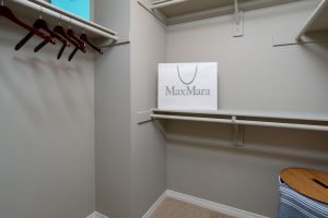 Large bedroom closet with shelves, poles, hangars, and laundry basket