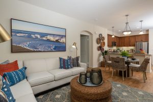 Cozy living room with sofa, chair, and wall art. Kitchen area with a dining table, bar stools, and modern appliances.